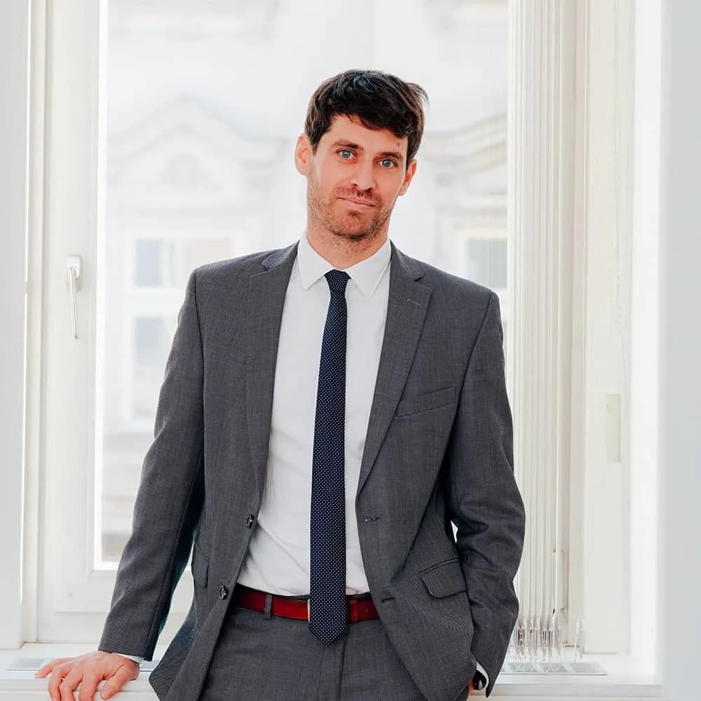 MMag. Daniel Köhle, Rechtsanwalt in Innsbruck, im grauen Anzug am Fenster seiner Kanzlei
